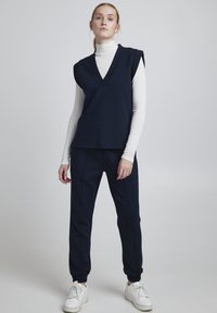 Top senza maniche blu navy con scollatura a V e spalle larghe, abbinato a pantaloni jogger coordinati con polsini elasticizzati e tasche laterali.