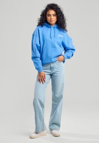 Light blue hoodie with a front pocket and drawstring, paired with light blue straight-leg jeans and white sneakers.