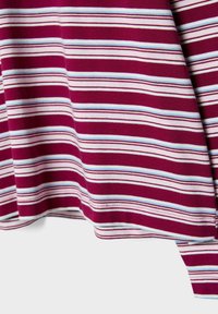 Tissu bordeaux avec un motif de rayures horizontales blanches, bleu clair et rouge foncé, drapé en plis doux sur un fond blanc.