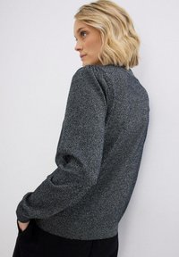Maglione grigio con texture, collo a giro e maniche a sbuffo. Polsini e orlo a coste. Tessuto morbido con un delicato luccichio. Tasche frontali visibili.