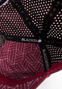 Maroon cap interior featuring a patterned lining with geometric designs, mesh panels with white dots, and a branded black strap.