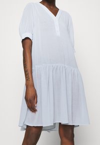 Světle modré šaty s výstřihem do V, podšitím knoflíky, krátkými puffovými rukávy a vrstvenou sukničkou. Vyrobeny z měkké, strukturované tkaniny.