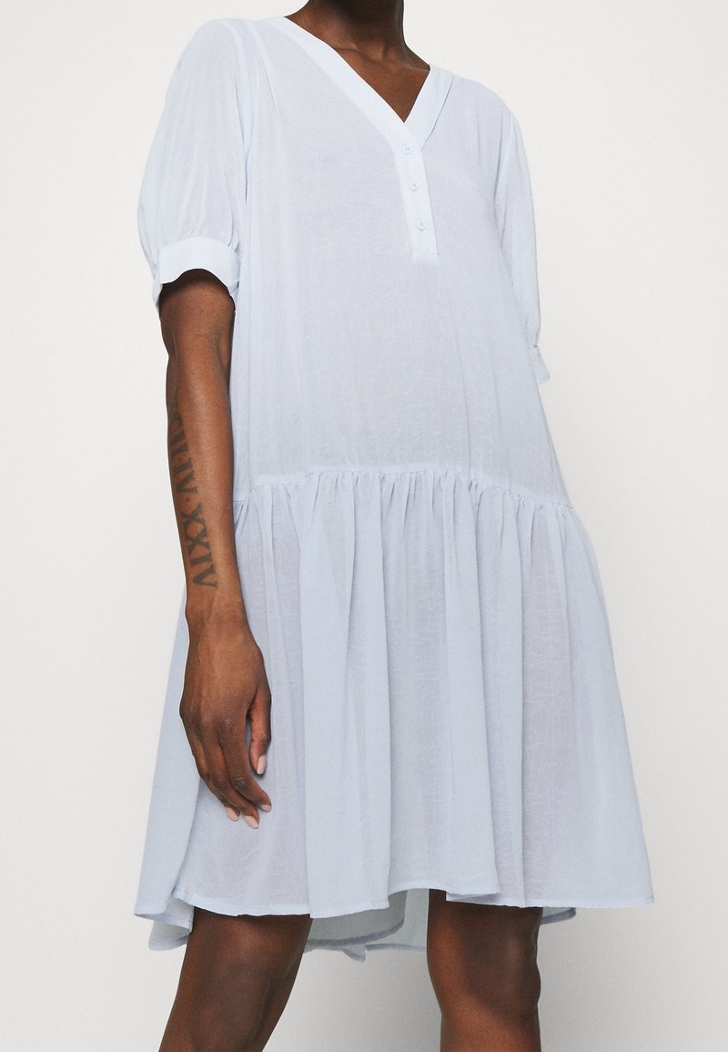 Světle modré šaty s výstřihem do V, podšitím knoflíky, krátkými puffovými rukávy a vrstvenou sukničkou. Vyrobeny z měkké, strukturované tkaniny.