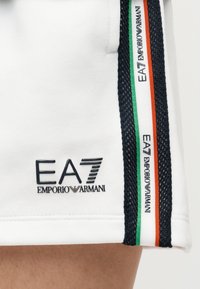 Λευκά σορτς με υφασμάτινη σκουρόχρωμη ρίγα και έγχρωμες αποχρώσεις (πράσινο, πορτοκαλί) στο πλάι. Διαθέτουν το λογότυπο EA7 σε μαύρο.