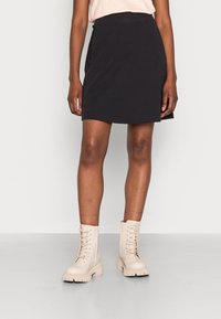 Falda negra hasta la rodilla hecha de una tela suave, con una textura lisa y una cinturilla elástica. Combinada con botas beige con cordones.