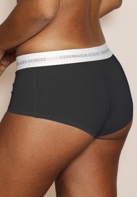 Black stretch shorts with a white waistband labeled "Copenhagen Studios," featuring a smooth texture and fitted design.