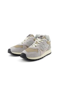 Sneakers grigio chiaro e beige in materiali scamosciati e mesh, con intersuola crema e suola in gomma nera. Presentano lacci e logo a contrasto.