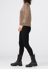 Braun- und Schwarz gemusterte Bluse, runder Ausschnitt, lange Puffärmel, kombiniert mit schwarzen Skinny Jeans und schwarzen Knöchelstiefeln mit strukturierten Sohlen.