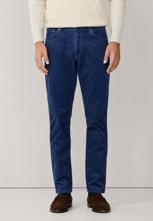 Dunkelblaue Cordhosen mit einem geraden Beinschnitt, Fünf-Taschen-Stil und einer weichen Textur, kombiniert mit einem hellbeigen Zopfmuster-Pullover.