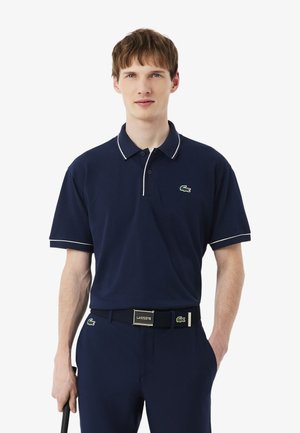 Polo blu navy con colletto bianco a contrasto, maniche corte e logo del coccodrillo verde ricamato sul petto.