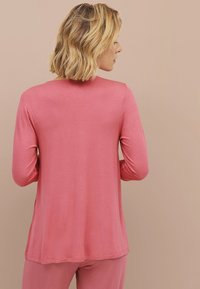 Langmouwen top in een zachte roze stof, met een ronde halslijn en een relaxte pasvorm, voorzien van zijsplitten voor een gemakkelijke beweging.