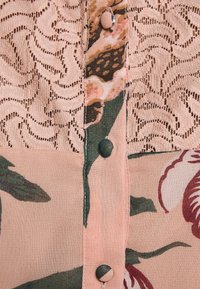 Blouse à motifs floraux en tissu rose doux. Détails en dentelle et boutons ronds. Accents de feuillage vert et de fleurs bourgogne.