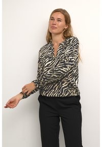 Langarmblouse in een zwart-wit zebra print met gouden accenten, met een V-hals en knoopdetails op de manchetten, gemaakt van lichte stof.