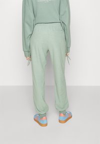 Ljusgröna joggers med resårmidja; mjuk textur. Kombineras med blå och rosa sneakers med gummisula.