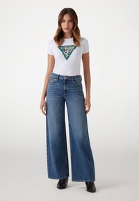 Hvid T-shirt med et grønt og dyreprint trekant design, parret med brede blå jeans, med høj talje og subtil fading.