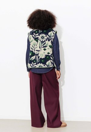 Gilet à motif floral avec base bleu marine, porté sur une chemise bleue ; pantalon ample bordeaux ; texture de tissu douce ; design décontracté.