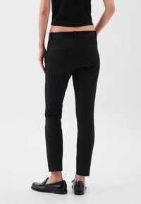 Fekete, karcsúsított nadrág sima textúrával, �öt zsebbel és övhurkokkal, fekete loaferekkel párosítva. Hátulnézetben látható.