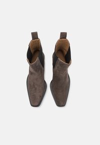 Botas de tobillo de ante marrón con paneles laterales elásticos negros, punteras afiladas y suela de goma negra, con un forro interior suave.
