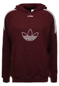 Maronfärgad Adidas-hoodie med en stor vit trefoil-logotyp på bröstet, vita tre ränder längs axlarna och ärmarna, framficka med kängurudesign och dragsko i huvan.