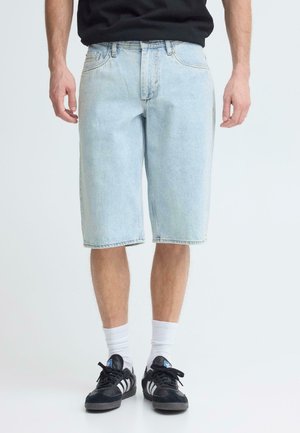 Lichtblauwe denim shorts met een losse pasvorm, voorzien van vijf zakken, gestikte details en een onafgewerkte zoom. Draag ze met zwarte sneakers en witte sokken.