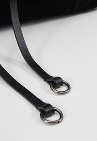 Deux sangles en cuir noir, chacune attachée à un anneau métallique, reposant sur une surface blanche.