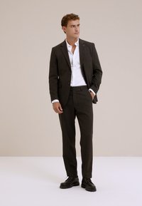 Mörkbrun kostym med en figursydd design, matchad med en vit skjorta. Slät textur, subtil glans och svarta skor fulländar outfiten.