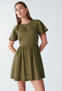 Oljčno zelena obleka iz lahkotnega materiala, ki ima kratke lepršave rokave, okrogel izrez in poudarjen pas s krožno krilo.