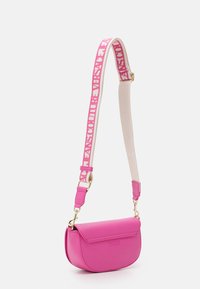 Rosa läder crossbody-väska med en rundad form, med en framflik, guldfärgade detaljer och ett brett axelband prytt med varumärkets text.