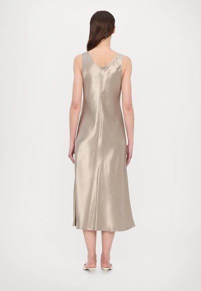 Satin midi-kjole i lys beige med v-ryg, uten ermer, sideslitt, og glatt tekstur, supplert med nøytrale farge hæler.