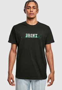Sort bomuld t-shirt med "BRONX" i hvid og grøn stiliseret tekst, korte ærmer, rund halsudskæring og afslappet pasform.