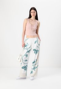 Light pink ribbed tank top with a tie front, paired with white wide-leg pants featuring turquoise floral patterns, and white sneakers.