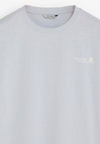 Camiseta de cuello redondo gris claro con pequeño texto blanco "CREATIVE STUDIO" y logotipo de calavera en el pecho superior izquierdo, con etiqueta Scalpers en el interior del cuello.