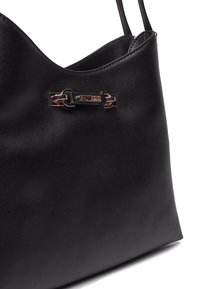 Sac à épaule en cuir noir avec une texture lisse, doté d'une plaque logo à l'avant et d'accents en métal doré.