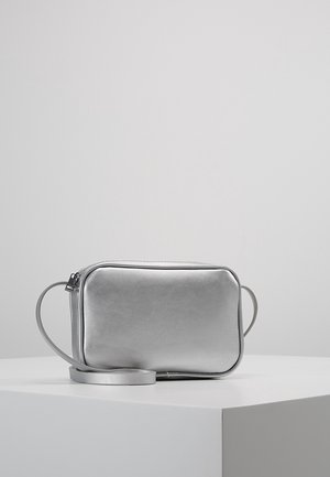 Mała, prostokątna, srebrna torebka na ramię z długim paskiem, gładką teksturą i zamkiem błyskawicznym, umieszczona na białym postumencie.