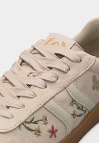 Baskets en daim beige avec lacets crème, broderie florale sur le côté, détail papillon et semelle en caoutchouc gomme.
