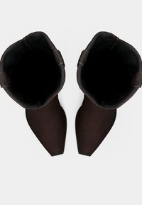 Ζευγάρι σκούρα καφέ δερμάτινων μπότες με μυτερές μύτες και θηλιές έλξης, που φαίνεται από πάνω με φόντο λευκό.