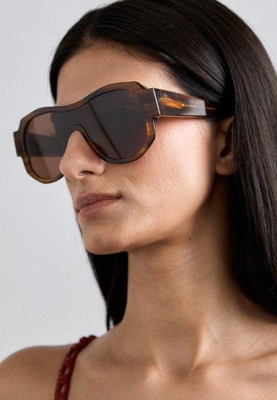 Tortoiseshell sunglasses with dark lenses, thick angled frames, and subtle metallic accents, showcasing a bold geometric design.