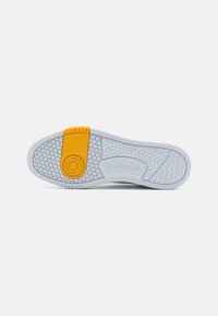 Suola di sneaker bianca con un motivo di presa testurizzato. Presenta un accento in gomma gialla vicino al tallone e il marchio Reebok di lato.