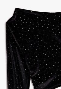 Top de terciopelo negro con mangas largas, adornado con tachuelas plateadas dispersas. Textura suave, diseño de escote amplio.