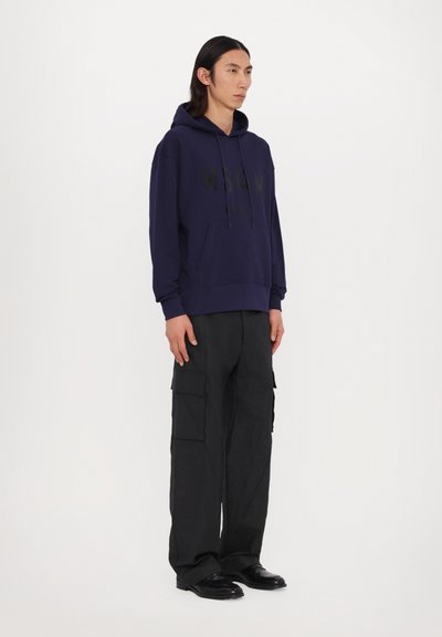 Felpa blu navy con tasca a marsupio frontale e stampa del logo nera, abbinata a pantaloni cargo neri dal taglio morbido e scarpe nere.