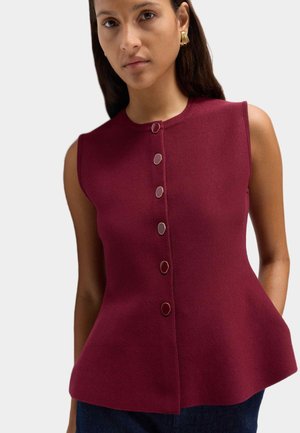Bordeaux ærmeløs top med tætsiddende liv og flagrende kant; har en lige halsudskæring og fem runde knapper nedad foran.