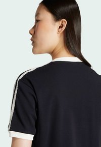 Black short-sleeve shirt with a crew neck, featuring a white trim and textured side accents. Soft fabric with a relaxed fit.