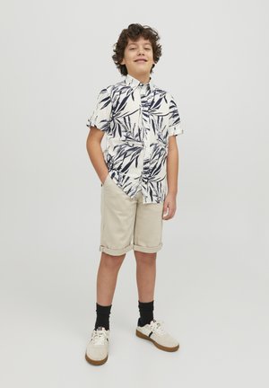 Camisa blanca de manga corta con un patrón de hojas en azul marino, pantalones cortos beige arremangados, calcetines negros y zapatillas crema con suelas marrones.