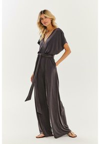 Sivý overal s hlbokým výstrihom do V, krátkymi rukávmi a opaskom v páse. Vyrobený z jemnej tkaniny, má široké nohavice a voľný strih.