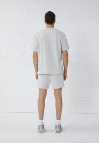 Light gray short-sleeve t-shirt and matching shorts, made of soft fabric. Casual fit, minimal design, worn with athletic shoes and socks.