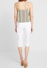 Gestreepte mouwloze top in geel, zwart en wit; gecombineerd met witte cropped broeken en witte hiel sandalen.