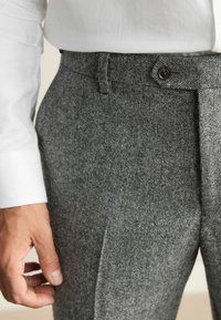 Gray, textured trousers made of a wool blend, with a single button waistband, side pockets, and a tailored fit.