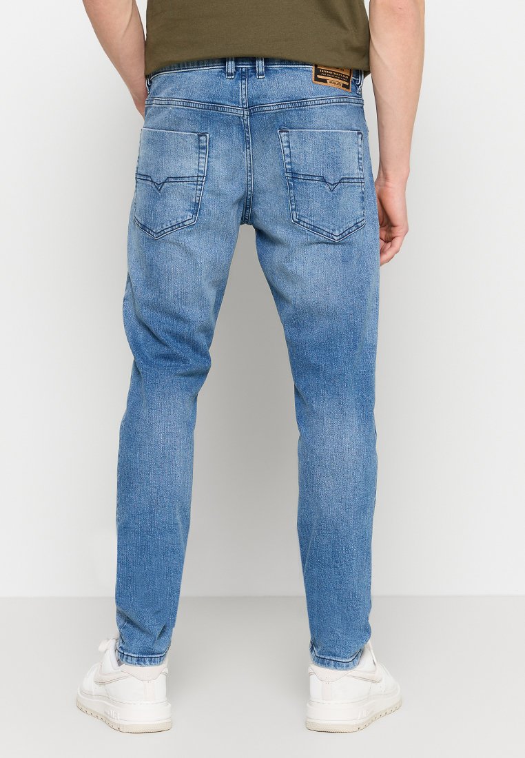 Jeans en denim bleu clair avec une coupe slim, dotés de poches arrière et d'un effet de lavage subtil. La ceinture est ornée d'une étiquette de marque.