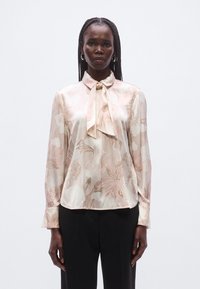 Hedvábná halenka s dlouhými rukávy, zdobená mašlí u límce. Květinový vzor v jemně růžové a krémové na světlém pozadí.