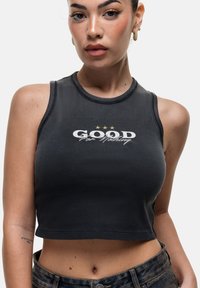 Top corto nero con texture a costine, caratterizzato da una stampa grafica bianca che recita "GOOD For Nothing" e tre stelle dorate sopra.